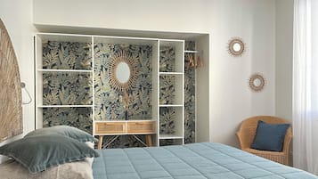 Een slaapkamer met een bed, een inbouwkast, een rieten stoel en decoratieve wandkunst.