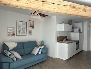 Un espace de vie moderne comprenant un canapé, un coin cuisine et des poutres en bois au plafond.