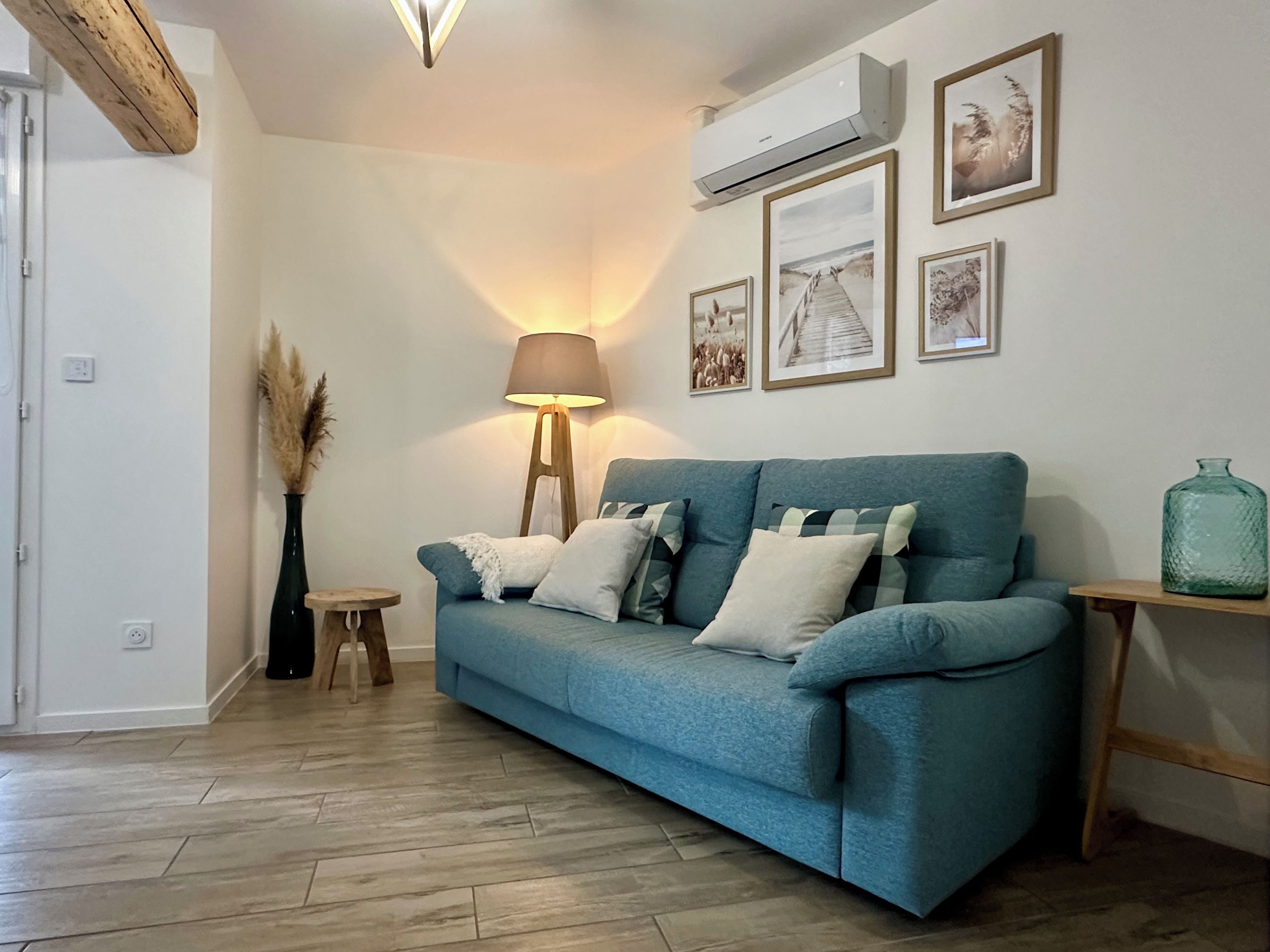 Een woonkamer met een blauwe bank, een vloerlamp en lijstjes aan de muur.
