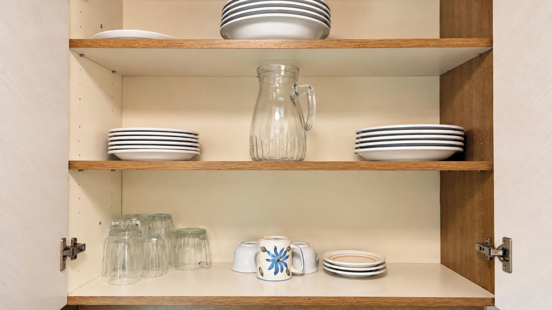 Un armario de cocina con repisas que sostienen platos, una jarra de vidrio y cristalería.