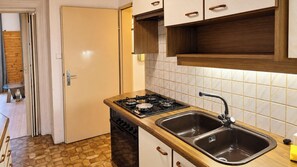 Cozinha com fogão a gás, pia dupla, armários de madeira e painel de azulejos.