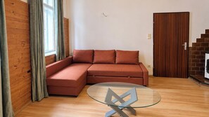 Una sala moderna con un sofá modular, una mesa de centro de vidrio, piso de madera, una pared de madera y una puerta.