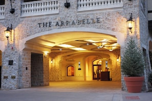Entrada de um edifício de pedra com a placa 'THE ARRABELLE', um caminho de acesso com portão e um vaso de planta.