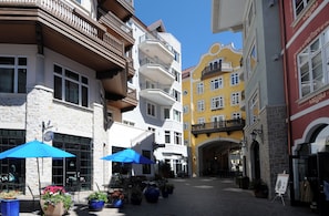 Rua com edifícios, mesas ao ar livre e plantas em vasos.