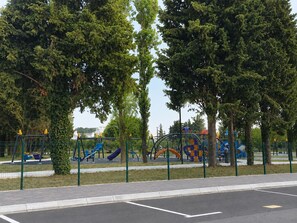 Parquinho com diversas estruturas de recreação, cercado por árvores e uma área isolada por cerca.