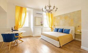 Ein Hotelzimmer mit einem Bett, einem runden Esstisch mit Stühlen, einer Kristallleuchtre und einem großen Fenster mit Vorhängen.