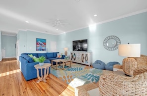 A living room with a blue sofa, a television, a white cabinet, and a decorative mirror. - Gulf-Front Luxury - 7BR - Salt Water Pool - Sleeps 22 (Gulf Shores)