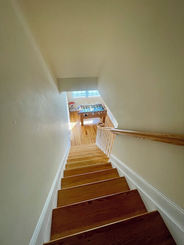 A wooden staircase leading to a room with a foosball table and a window. - 4 Bedroom Rooftop Retreat in beautiful Seaside Heights (Seaside Heights)