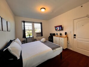 Een hotelkamer met een bed, een bureau, een televisie, een magnetron en een deur.
