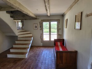 A room with a wooden staircase, a door leading outside, and a bed with a red and white striped bedspread. - New Listing (Caylus)