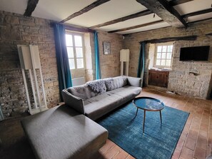 A living room with a sofa, a coffee table, and a television mounted on a stone wall. - New Listing (Caylus)