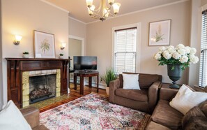 Ein Wohnzimmer mit Kamin, Fernseher, Sofa, Teppich und einem Blumenstrauß.
