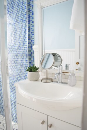 Ein Badezimmer mit weißem Waschbecken, einem runden Spiegel, einem Topfpflanze und einer blaugefliesten Wand.