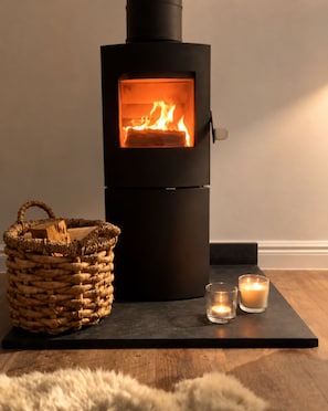 A wood-burning stove with a fire, a woven basket, and two candles on a black platform.