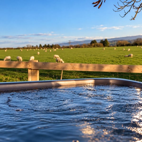 A hot tub with a wooden fence in the foreground and a green field with sheep in the background.