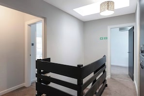Une pièce avec un lit superposé, un luminaire au plafond, une porte portant un panneau indiquant la sortie de secours et un sol recouvert de moquette.