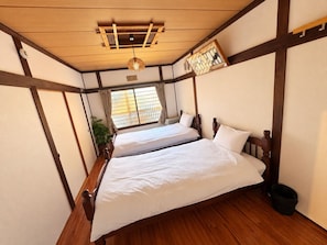 A traditional Japanese-style room with two wooden beds, a wooden ceiling, and a window with curtains.