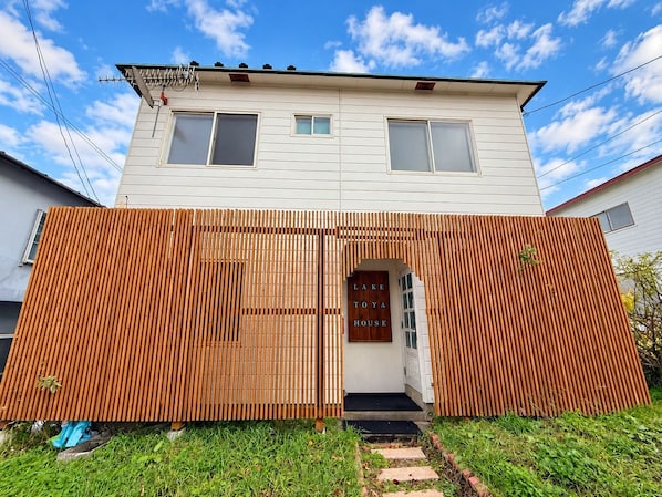 A two-story house with a wooden fence in front, a visible door, and a small step leading to the entrance.