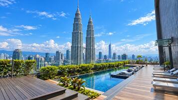 Ein Poolbereich auf dem Dach mit Blick auf die Petronas Towers, umgeben von Grünflächen und Liegestühlen.