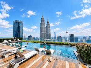 Un espace piscine aménagé sur le toit, avec des chaises longues et une vue sur les tours Petronas.