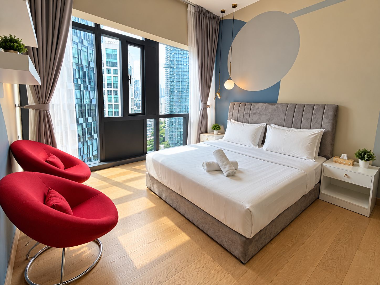 A modern hotel room with a large bed, a red chair, and a view of the cityscape through the window.