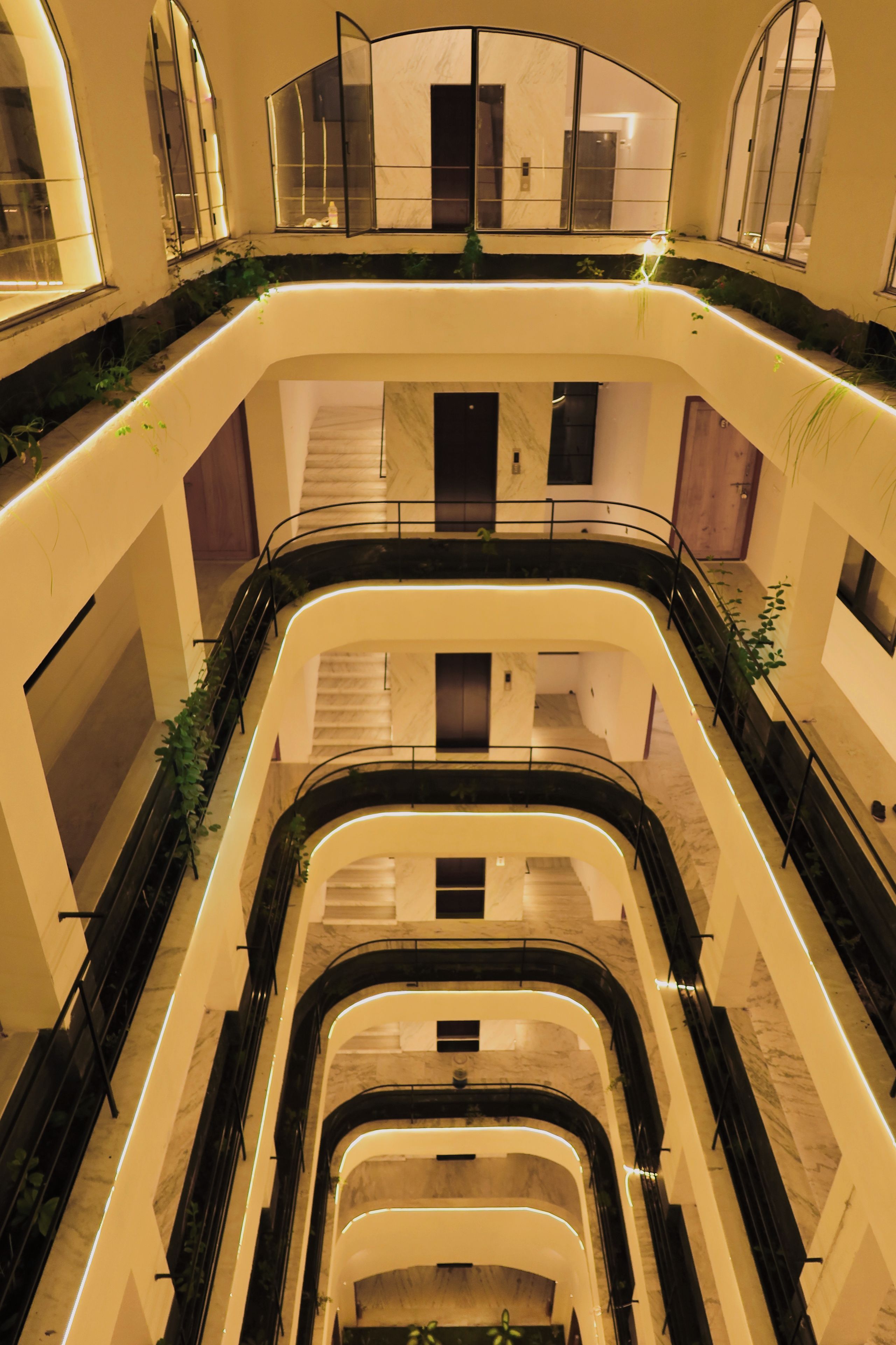 Un atrio de varios niveles con una escalera central, barandillas de vidrio y plantas.