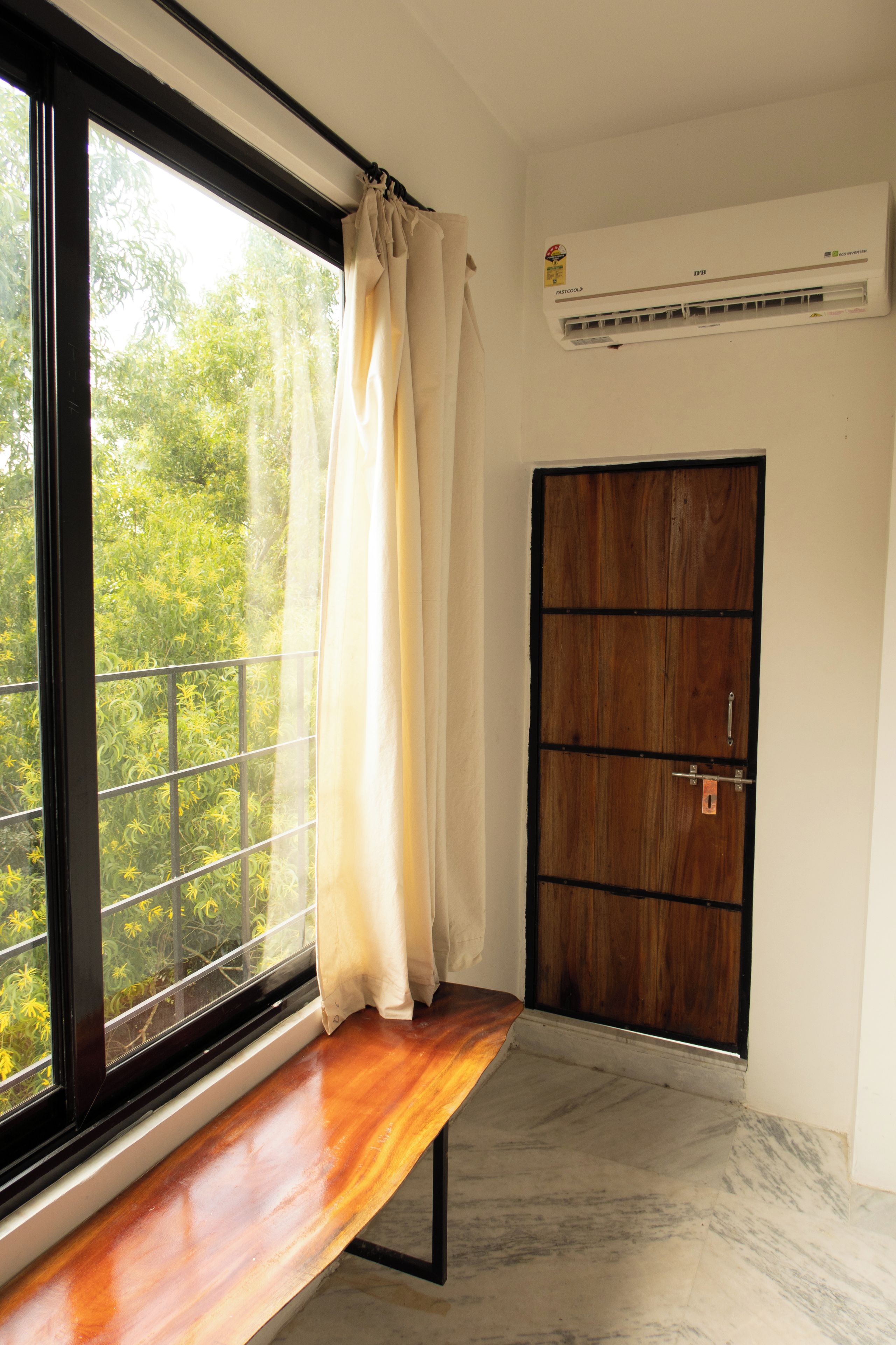 Une pièce avec un banc en bois près d’une fenêtre, une porte et un appareil de climatisation.
