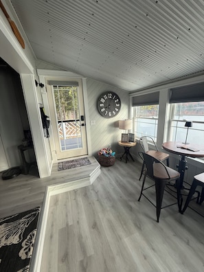 Une pièce avec un plancher en bois, une horloge murale, une table à manger avec des chaises, une lampe et un panier.