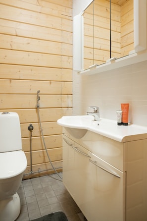 A bathroom with a wooden wall, a white sink, a mirror, and a toilet.