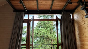 A room with a wooden ceiling, a large window with curtains, a sofa, and a view of trees outside.