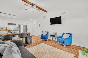 Un salon moderne comprenant un canapé, deux fauteuils bleus, une table basse et un téléviseur à écran plat fixé au mur.