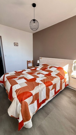 Une chambre avec un grand lit, une table de chevet, une chaise, un luminaire suspendu et un tableau au mur.
