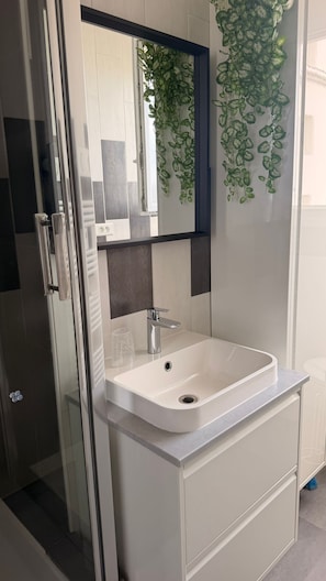 Une salle de bain avec un lavabo blanc, un miroir et des plantes vertes.
