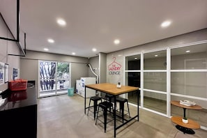Un interior moderno con una mesa de madera y taburetes negros, una pequeña mesa redonda y un letrero que dice 'The Laundry Lounge'.