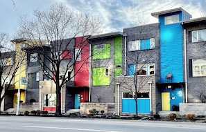A row of modern multi-story buildings with distinct color accents on the facades. - Walkable downtown Dayton MCM townhome with garage and balcony! (Dayton)