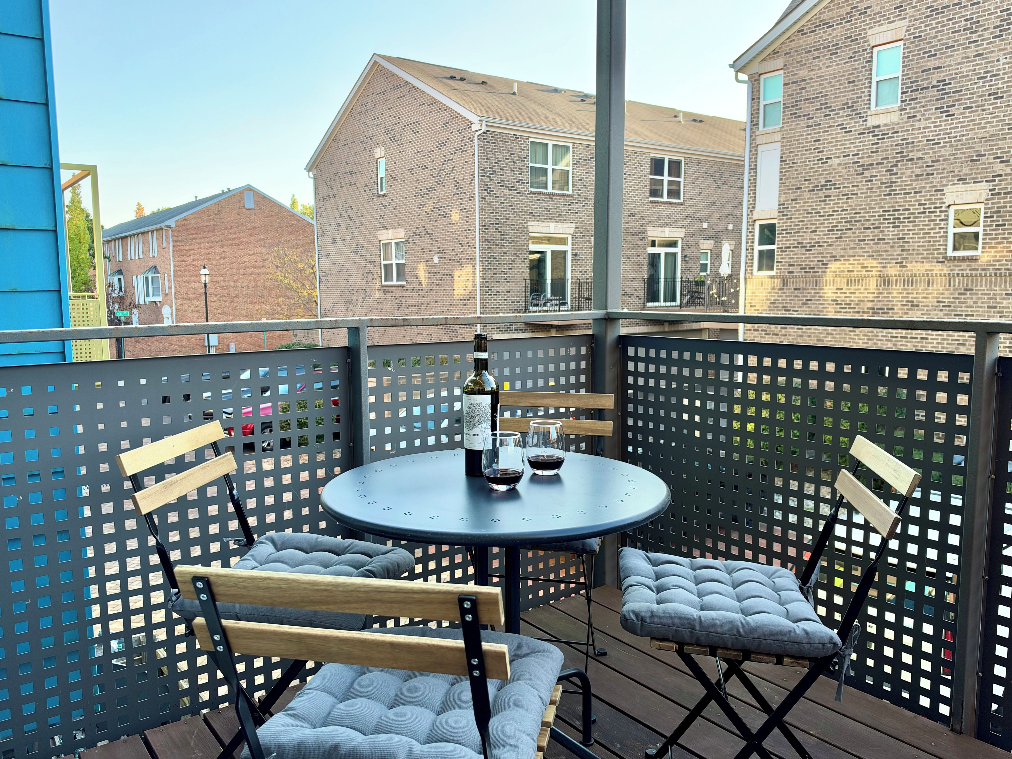Un balcon avec une table ronde, deux fauteuils confortables et une bouteille de vin.