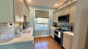 A modern kitchen with a large window, stainless steel appliances, and light-colored cabinetry.