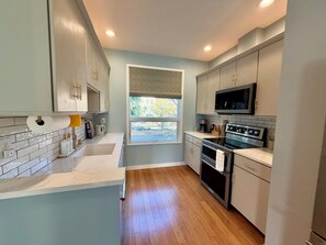A modern kitchen with a large window, stainless steel appliances, and light-colored cabinetry. - Walkable downtown Dayton MCM townhome with garage and balcony! (Dayton)