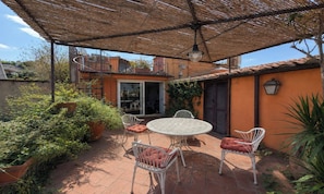 Eine Terrasse im Freien mit einem runden Tisch und vier Stühlen, umgeben von Blumentöpfen und einer Pergola.