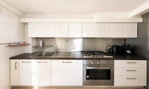 Eine moderne Küche mit weißen Schränken, einer Edelstahlspüle, einem Gasherd und einem Backofen.