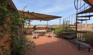 Eine Terrasse im Freien mit Tisch und Stühlen, umgeben von Pflanzen und Blick auf die Stadt.