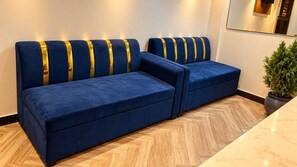 A blue sofa with gold accents in a modern room with a herringbone floor pattern. - Classic Hotel Blue Stone (Mumbai)