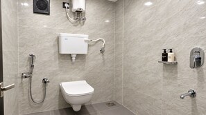A modern bathroom with a toilet, shower, and a toilet paper holder with toiletries. - Classic Hotel Blue Stone (Mumbai)