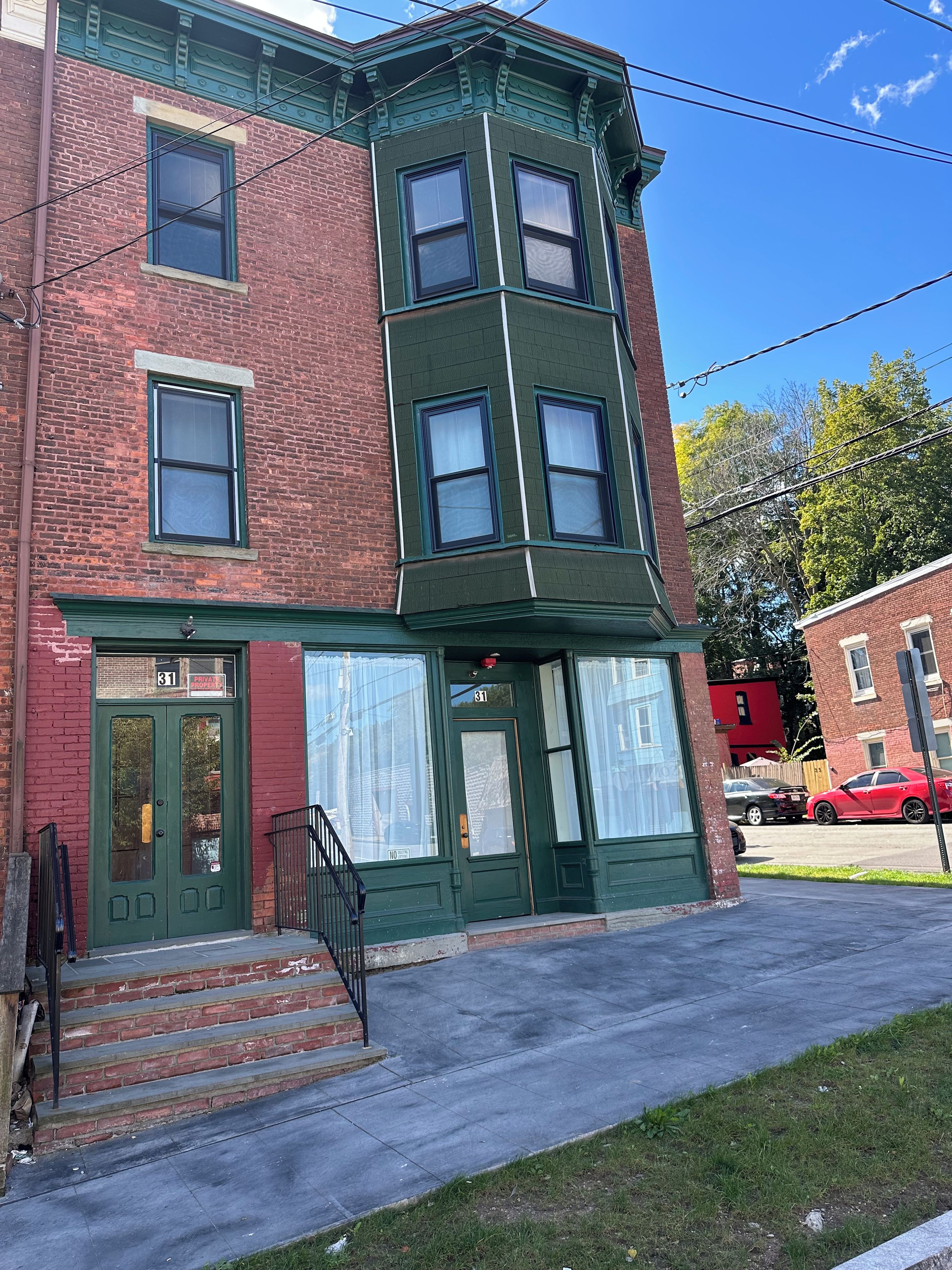 A multi-story building with a green awning, a brick facade, and a set of stairs leading to the entrance.