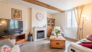 Een woonkamer met een televisie, open haard, bank en een klok aan de muur.