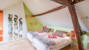 Een slaapkamer met een schuine kap, houten balken, een bed met kussens, een nachtkastje en een spiegel.