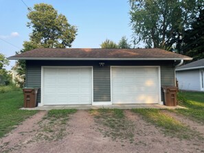 Un garage pour deux voitures, avec un toit brun, une allée en béton et deux poubelles brunes placées de part et d’autre.