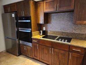 A kitchen with wooden cabinets, stainless steel appliances, and a granite countertop. - Hilton Grand Vacation Bay Club-Waikoloa - VILLA - XMAS - Dec 19 to Dec 26 2026 (Waikoloa Village)