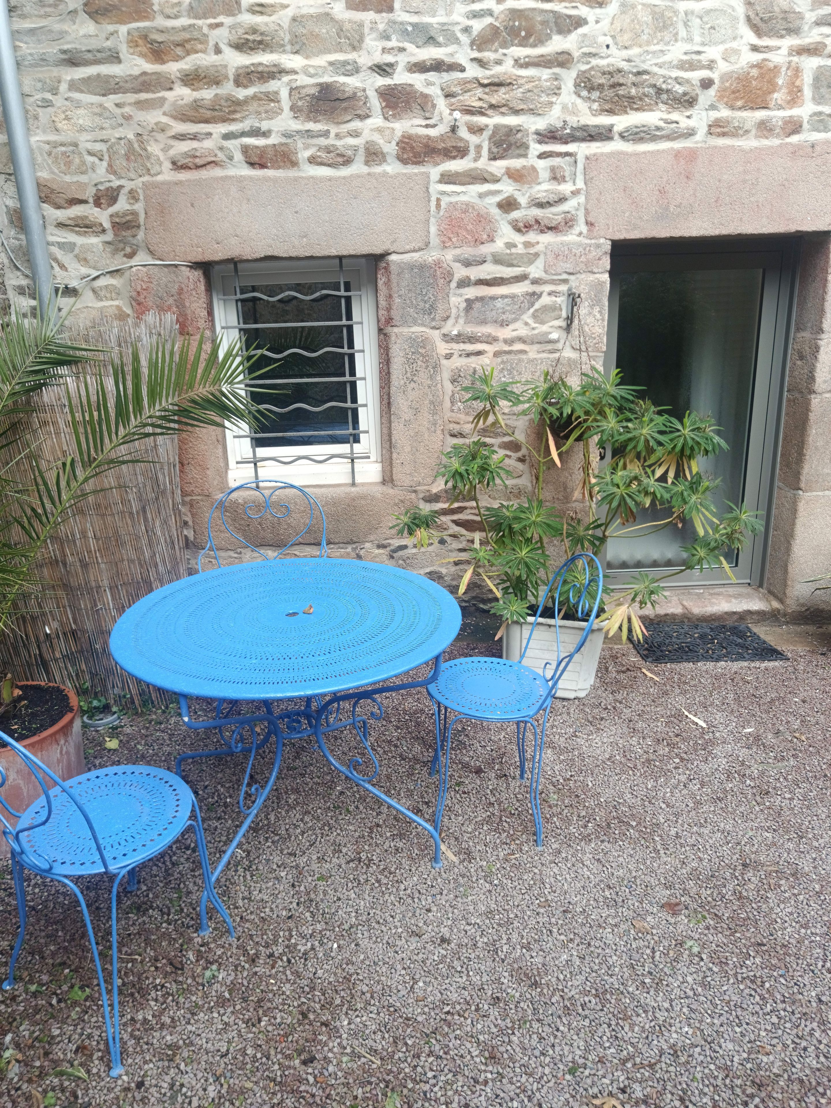Un bâtiment en pierre avec une table ronde en métal bleu et quatre chaises assorties.
