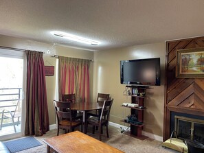 Una sala de estar con televisor, chimenea, mesa de comedor con sillas y ventana con cortinas.